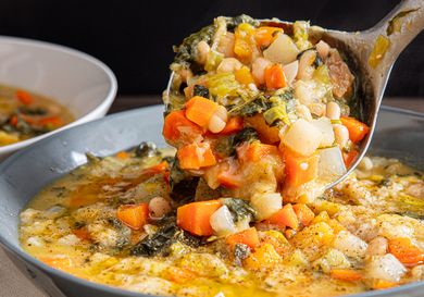 A ladle lifting thick and chunky vegetable soup from a bowl