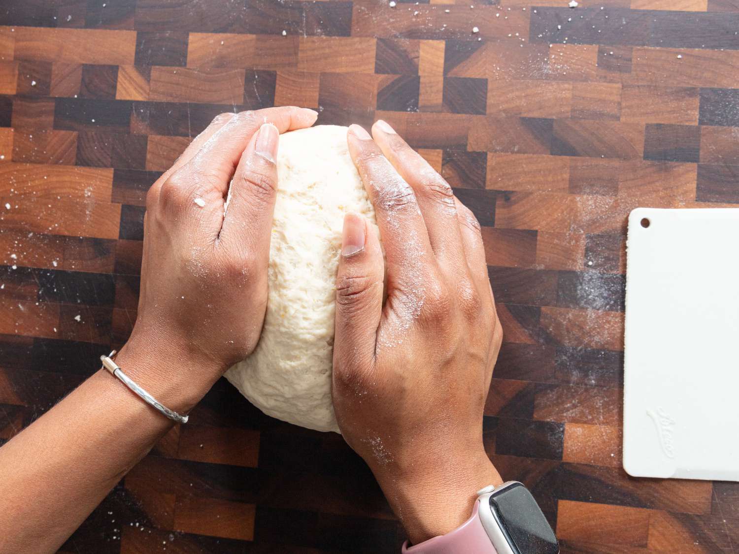 Hands holding and forming ball shape from dough on a chopping block 