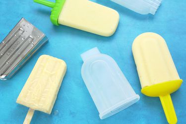Assorted popsicle molds and ready popsicles placed on a blue surface