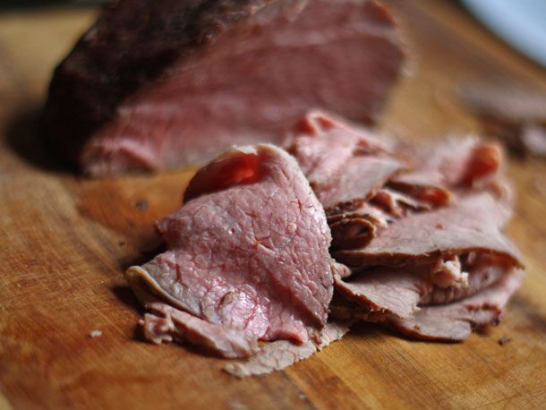 Thin slices of medium-rare beef piled on a cutting board. The roast they were carved from is out of focus in the background.