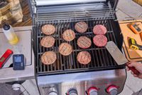 A hand using a metal spatula to flip patties on the Weber Spirit EP-435 Gas Grill