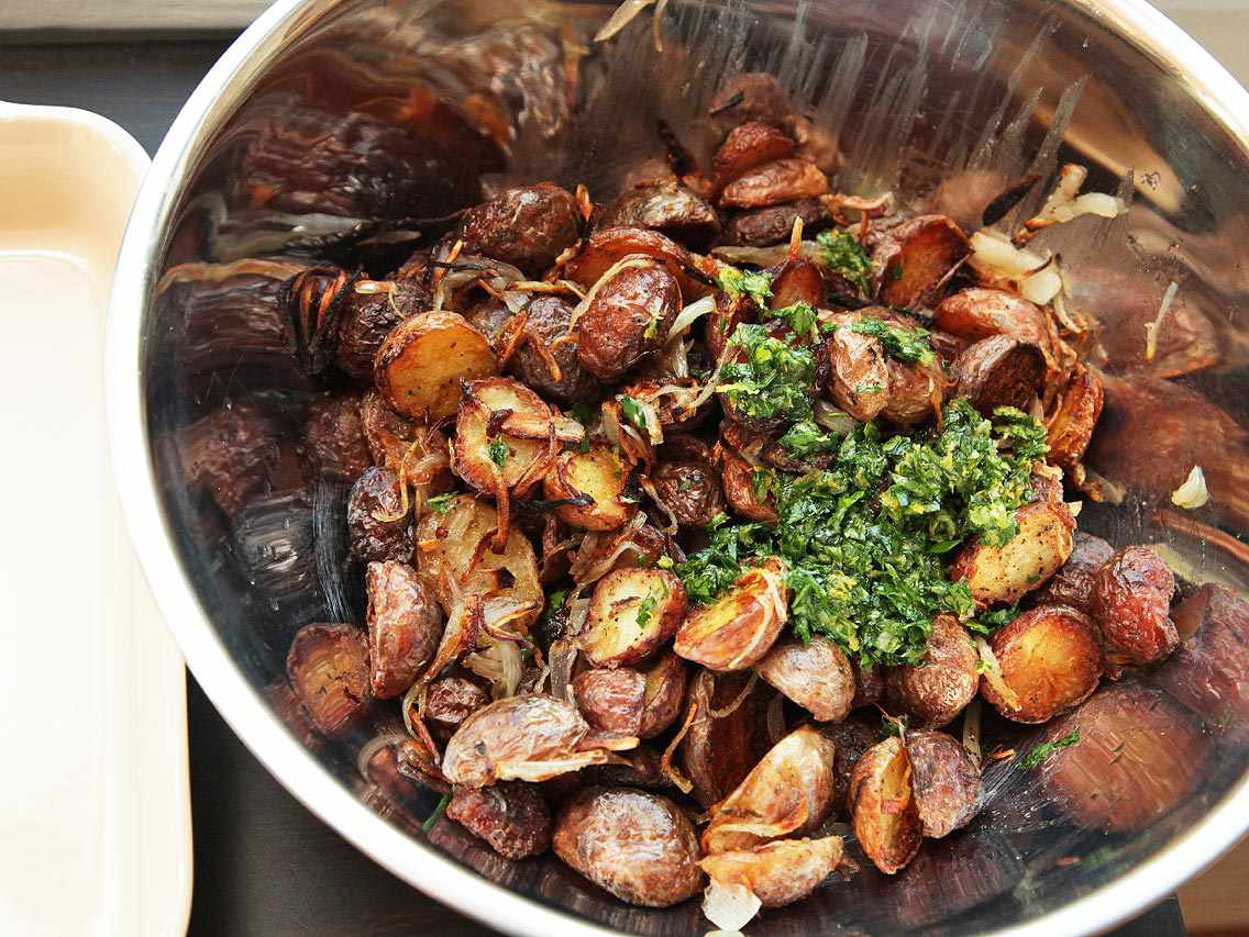 Large silver mixing bowl filled with roasted potatoes and chopped fresh herbs.