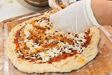 Pizza dough topped with barbecue pizza sauce and cheese is topped with pulled pork before grilling.