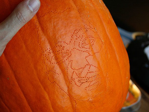 An outline of a face made by poking a series of holes into the surface of a pumpkin
