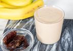 A bananadate smoothie in a glass bananas and dates beside it