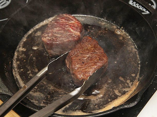 Searing two small steaks in a hot cast iron skillet.