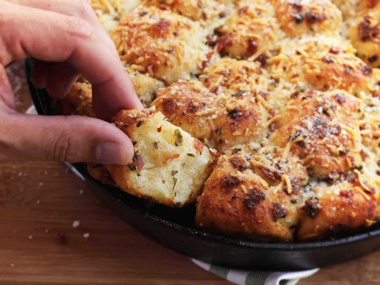 Hand pulling a pepperoni garlic knot out of a cast iron pan