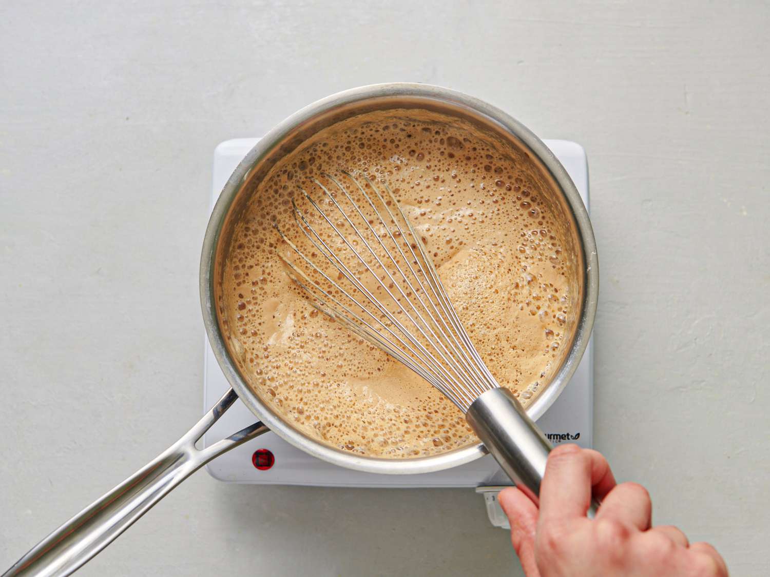 Beer, milk, Worcestershire sauce, and mustard being whisked together in a stainless steel saucepan.