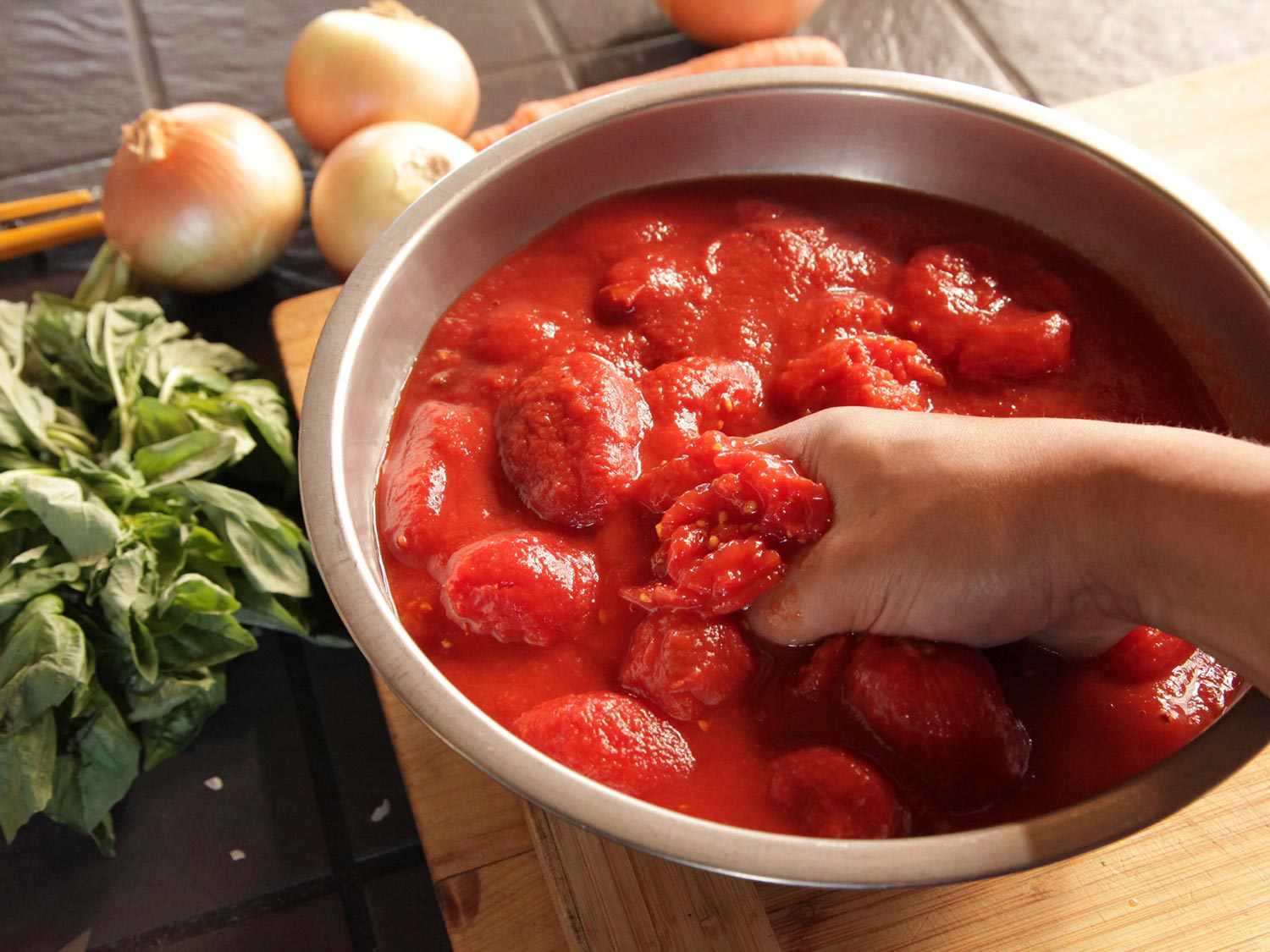 Hand-crushing canned tomatoes in metal bowl