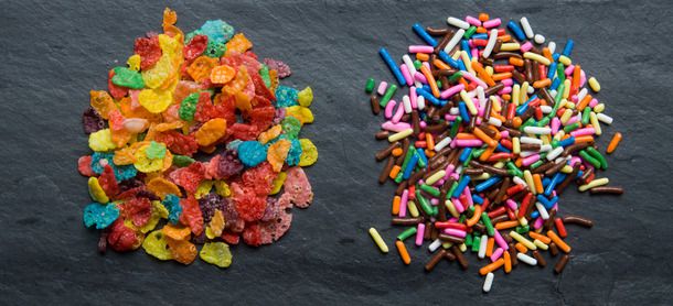A small pile of fruity pebble cereal next to a pile of assorted color sprinkles.