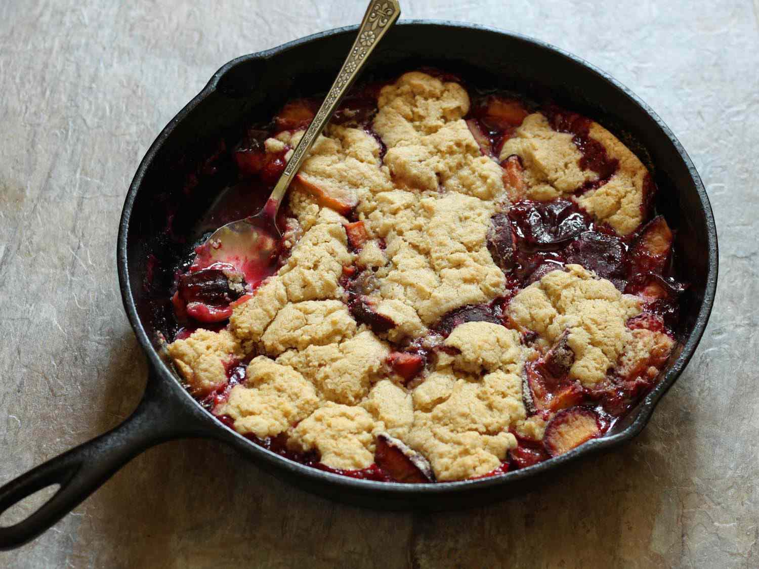 Gluten-free plum cobbler in a small cast iron skillet, with a spoon sticking out