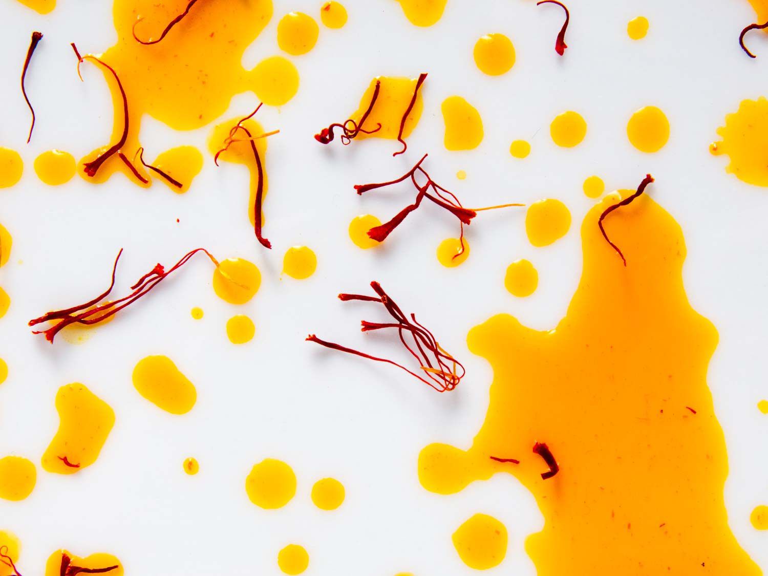 Close-up of saffron threads and splatters of saffron "tea" on a white surface.