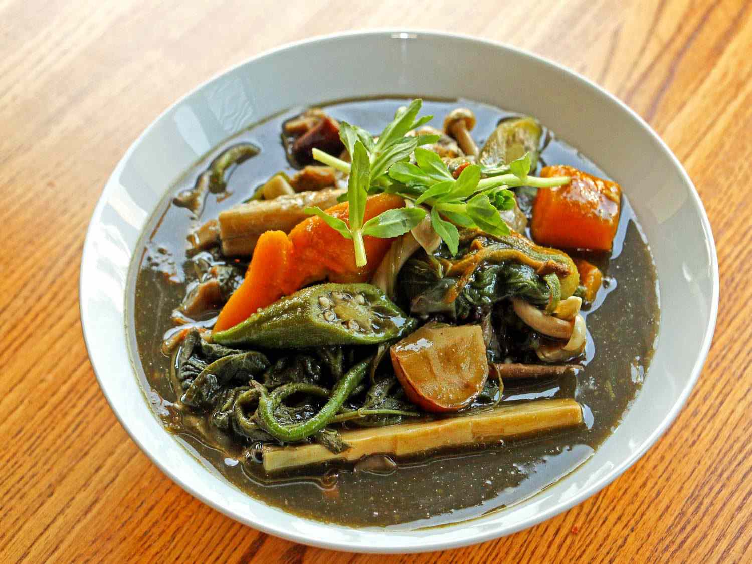 A bowl of gaeng naw mai: a dark-green broth with bamboo shoots, green yanang leaves, and other vegetables and herbs.
