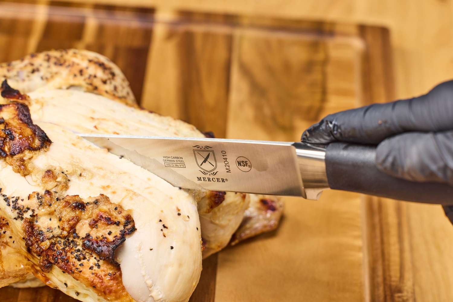 A person slices a chicken with the Mercer Culinary 10-Inch Carving Knife