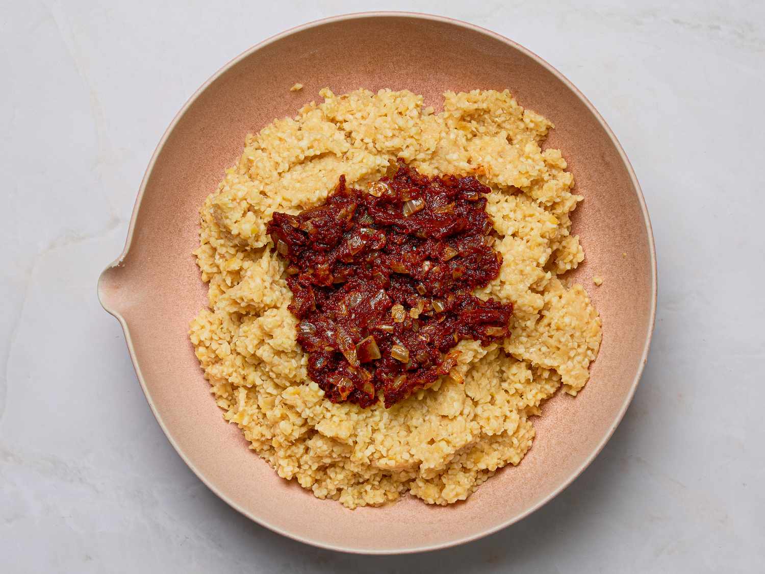 A dish featuring Turkish red lentil kfte in preparation topped with a tomatobased mixture