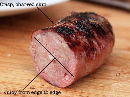 A piece of sausage on a wooden cutting board, with labels pointing out a center that's juicy throughout and a crisp, charred skin