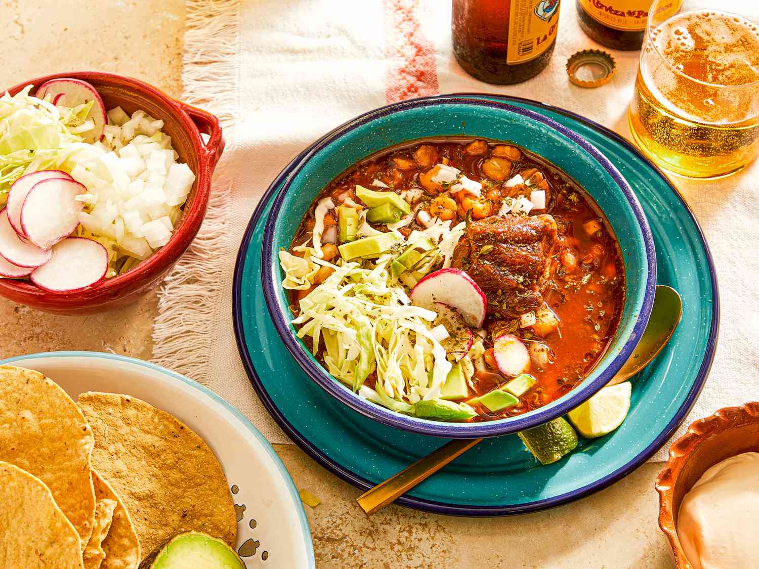 Pozole Rojo served in a turquoise bowl surrounded by bowls of toppings