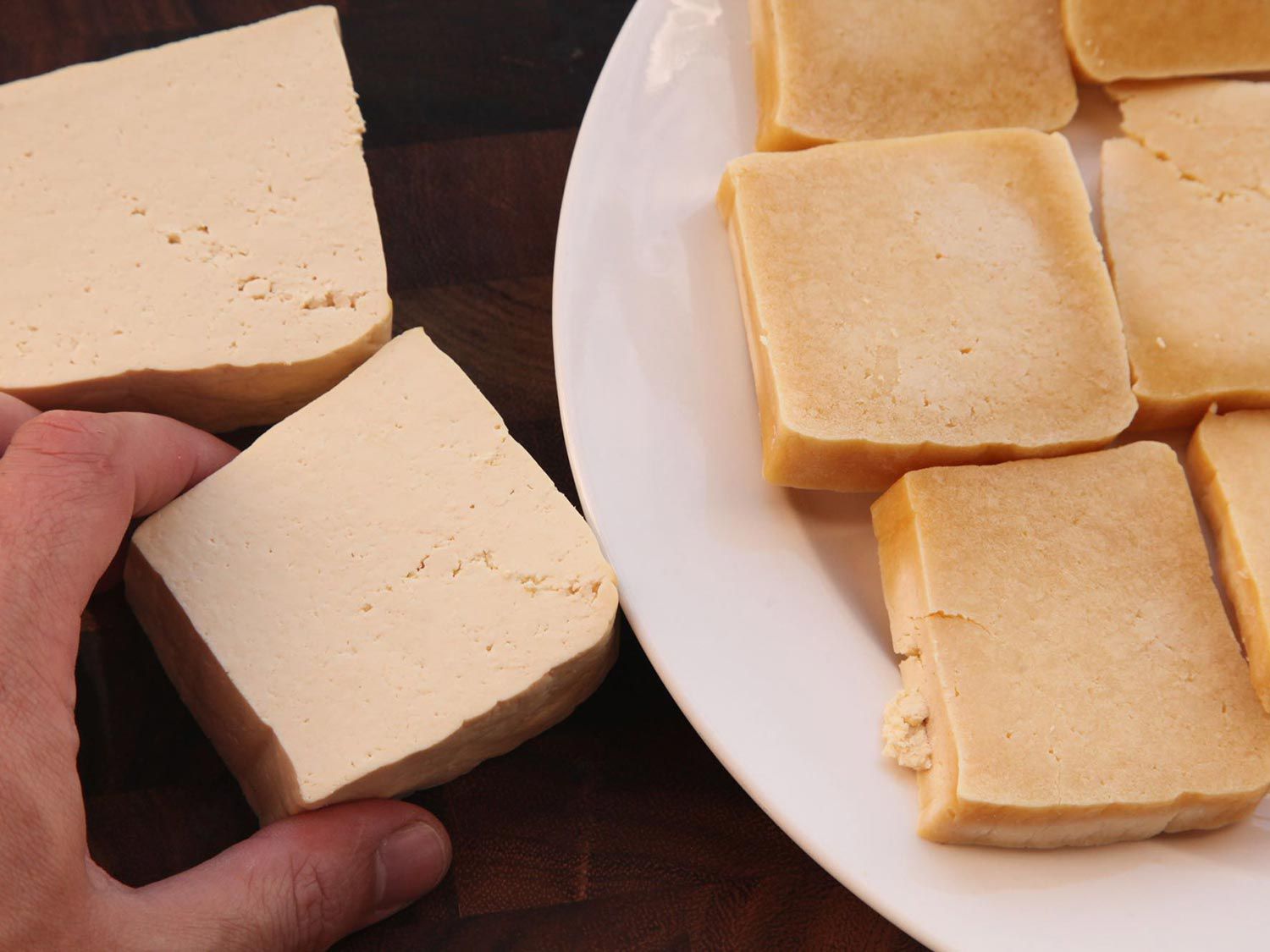 Author comparing fresh tofu to a plate of frozen tofu slabs. The frozen tofu has darkened significantly.