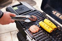 A person cooking burgers and corn on the cob on the Masterbuilt portable charcoal grill.