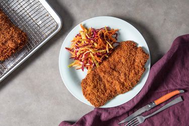 Overhead view of pork schnitzel, served on a plate with a colorful vinegar-based coleslaw.
