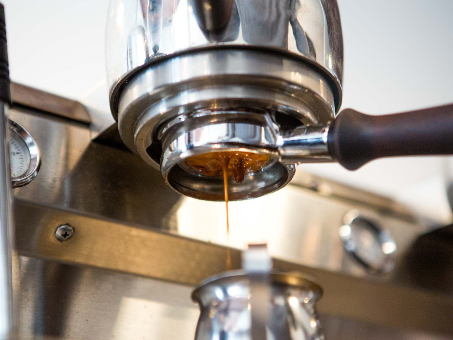 Espresso pours from the machine's portafilter into a small pitcher.