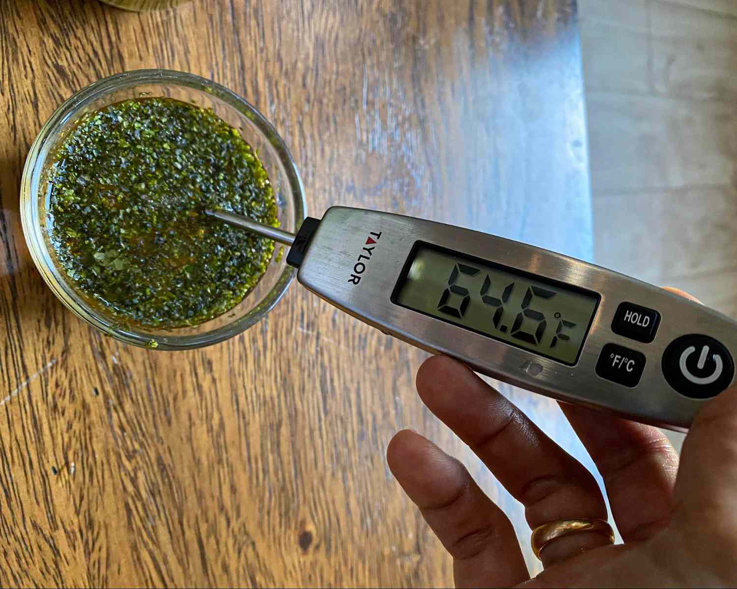 A digital thermometer shows 646F while inserted into a glass container of blended herb mixture on a wooden surface
