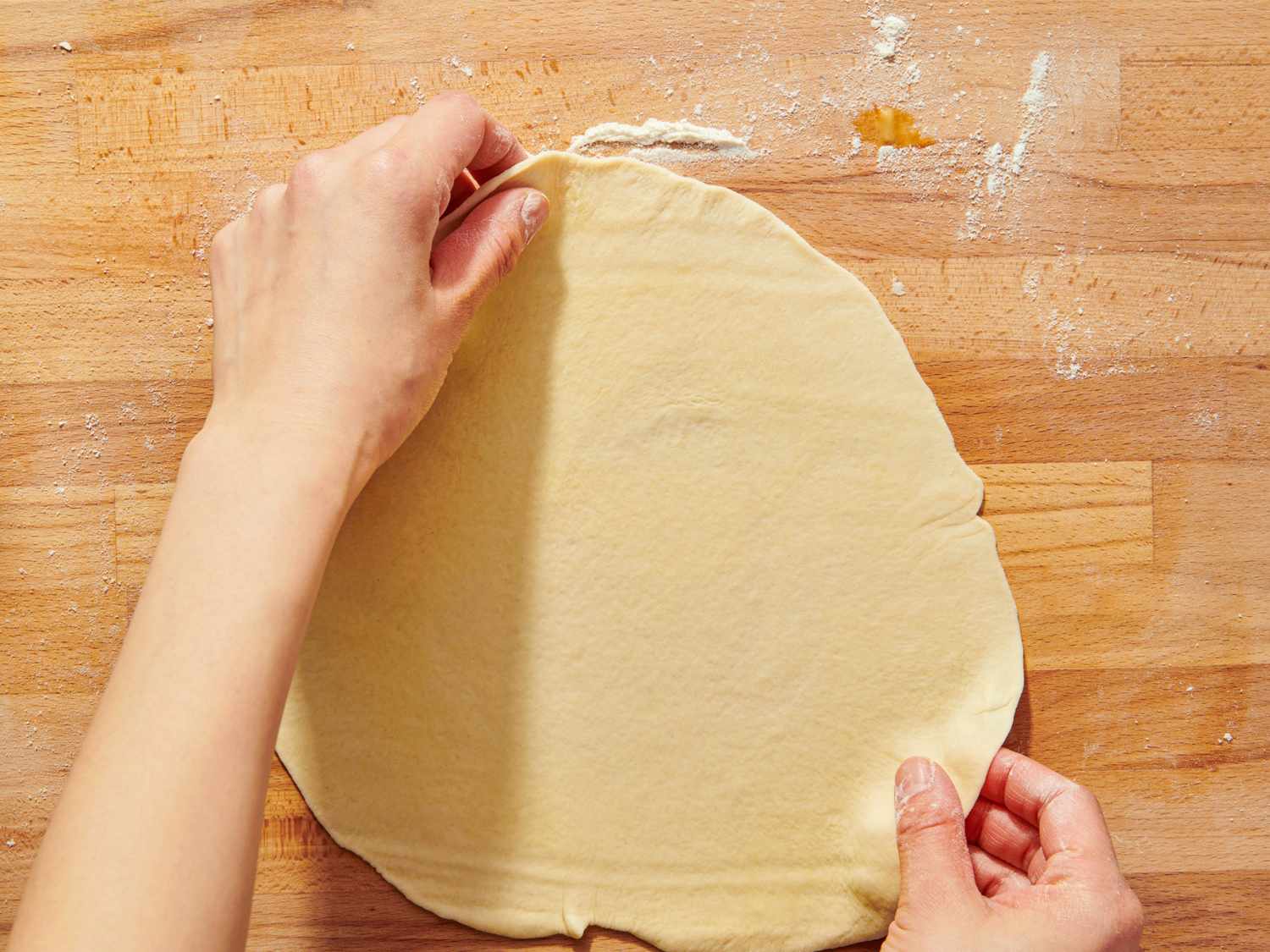 Hands rolling out dough on a surface
