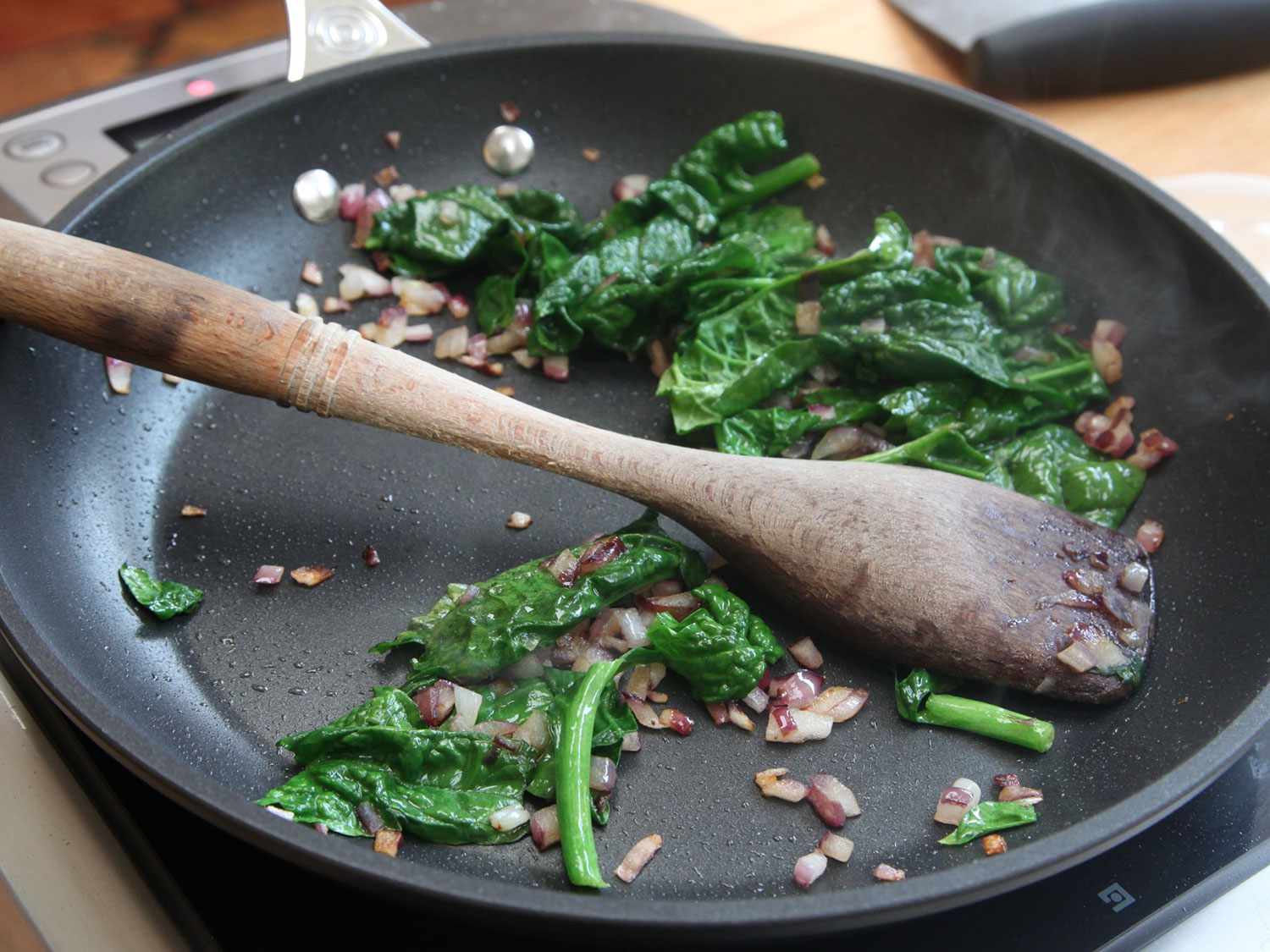 Sautéing spinach and red onion in a non-stick skillet with a wooden spoon