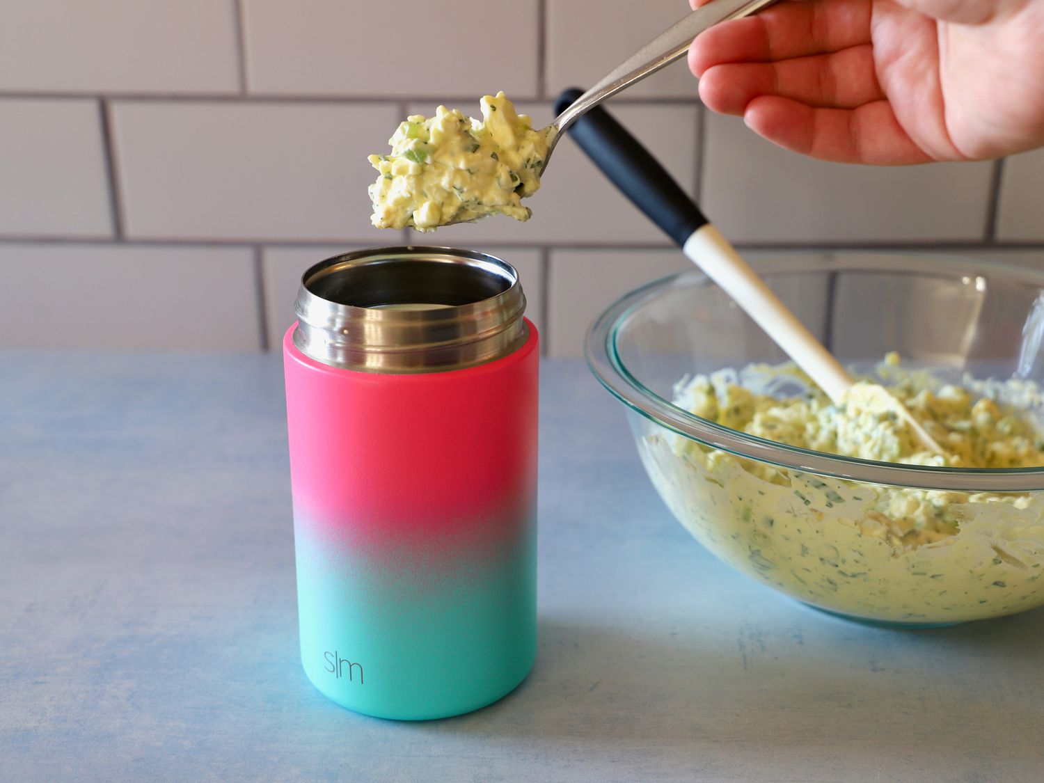 a person filling thermos with egg salad