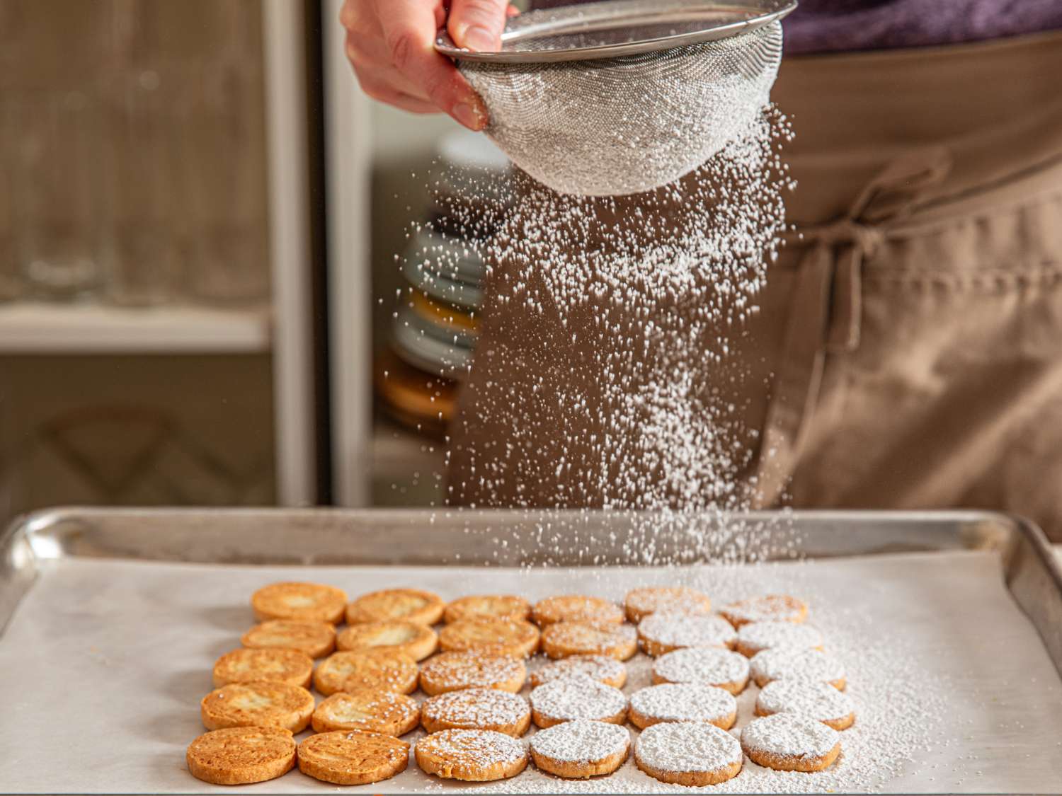 Sifting powdered sugar onto a tray of cookies