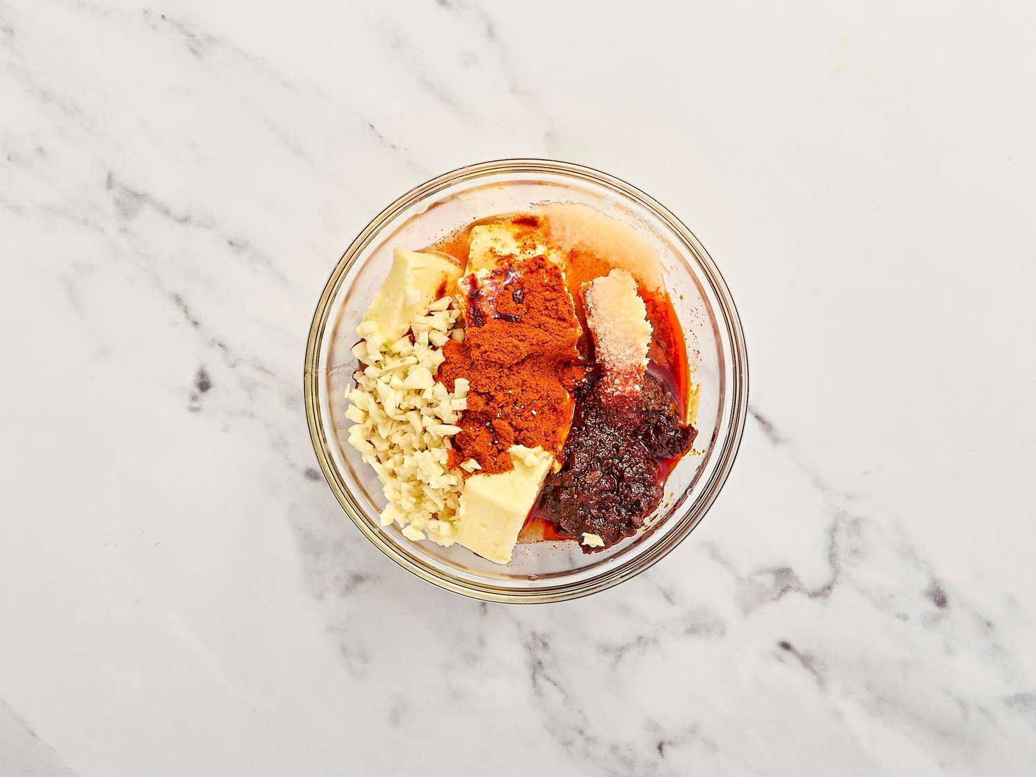 Bowl containing garlic, paprika, butter, seasonings, and harissa paste on a marble surface