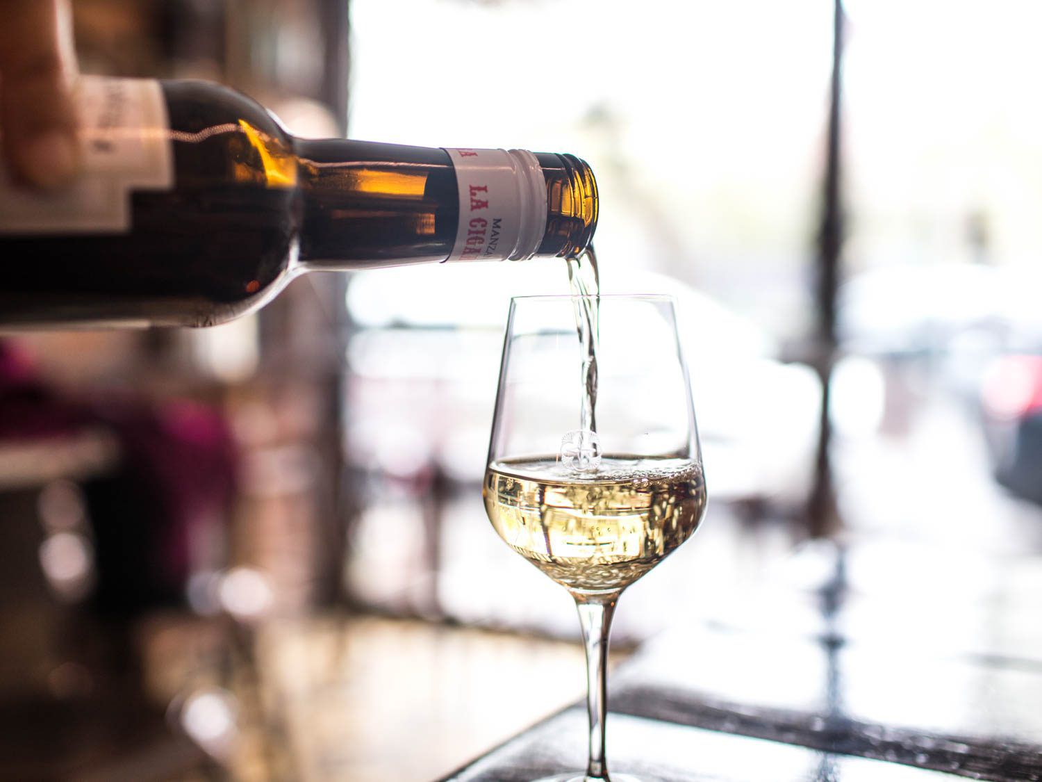 A hand pouring from a bottle of pale Manzanilla sherry into a wineglass