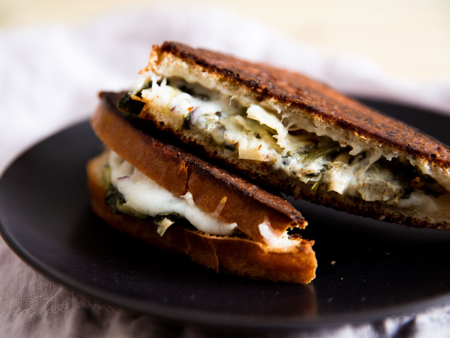 Closeup of a halved and shingled Spinach and Artichoke Grilled Cheese Sandwich, served on a black plate.