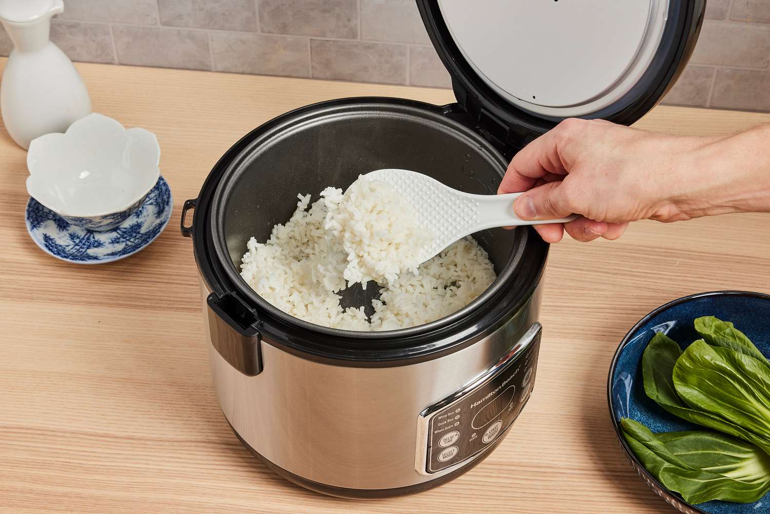 a ricer cooker with a person using a paddle to retrieve a scoop