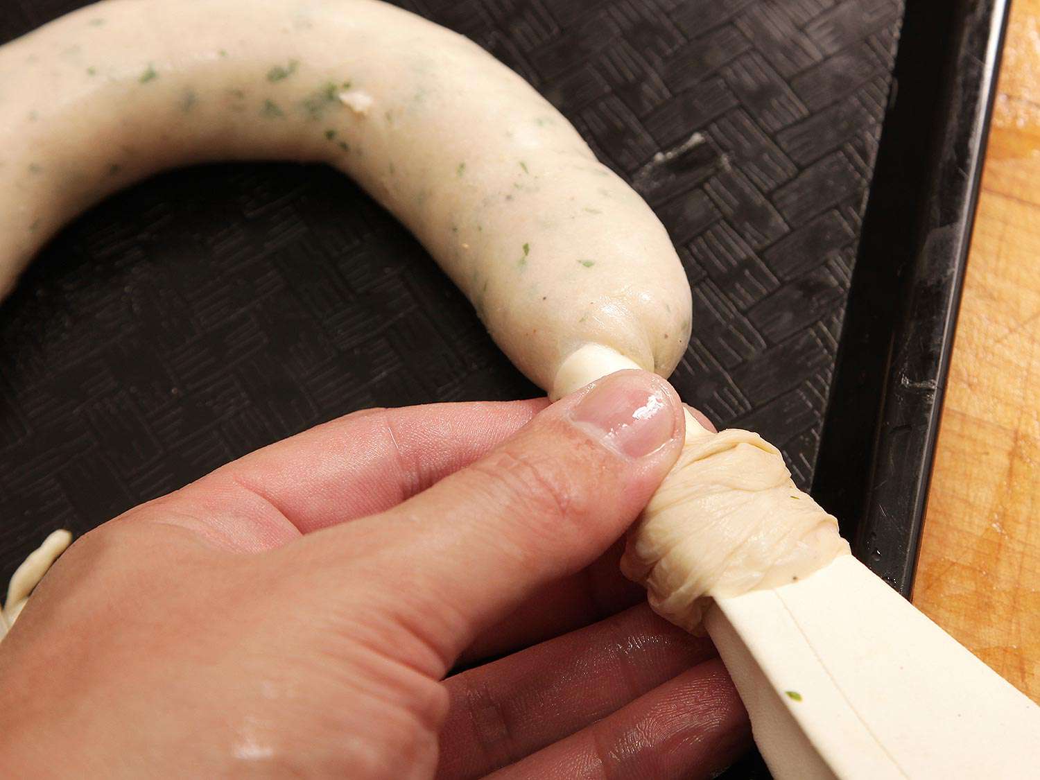 The author holds the tip of the pastry bag, allowing them to control the length of casing that is let out as the bag expels forcemeat.