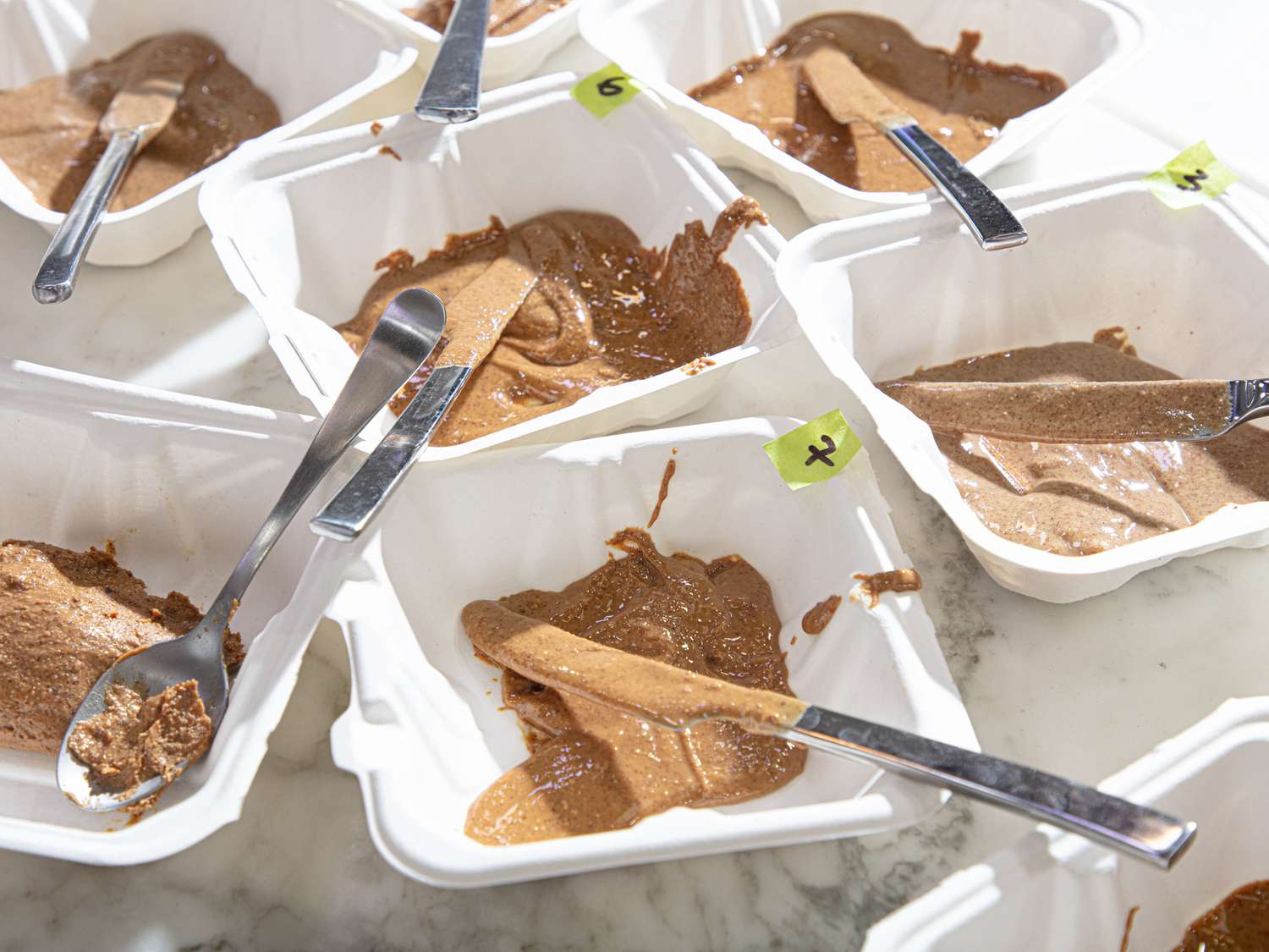 Multiple plastic trays filled with samples of almond butter and silver tasting spoons