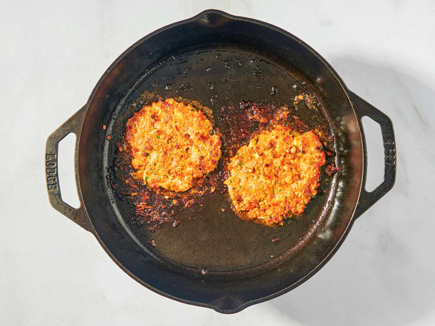 Two turkey burger patties cooking in a cast iron skillet