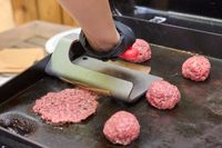 A person makes hamburgers on the Weber Slate 22 inch Rust-Resistant Tabletop Griddle