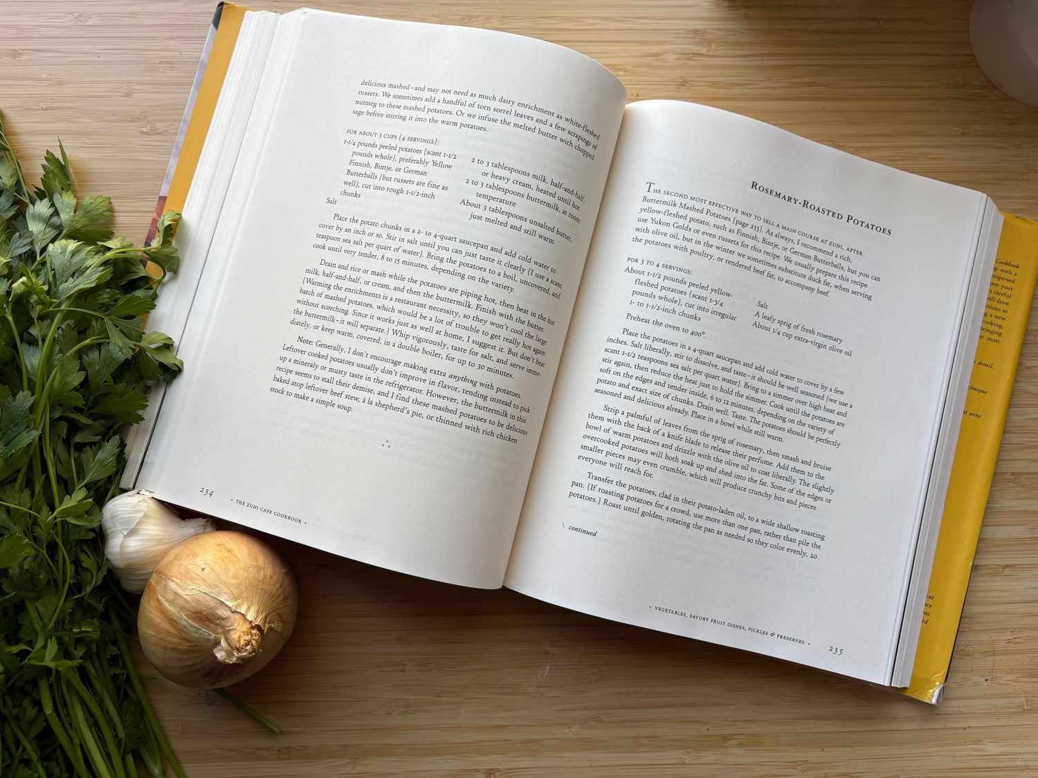 Open cookbook on a wooden surface next to herbs and an onion