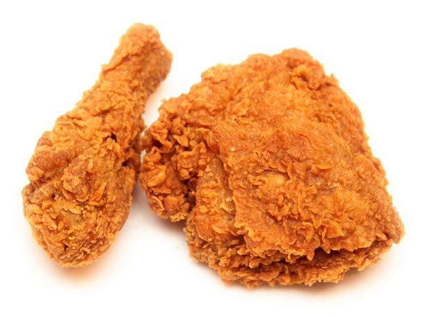 Two pieces of fried chicken resting on a white surface. 