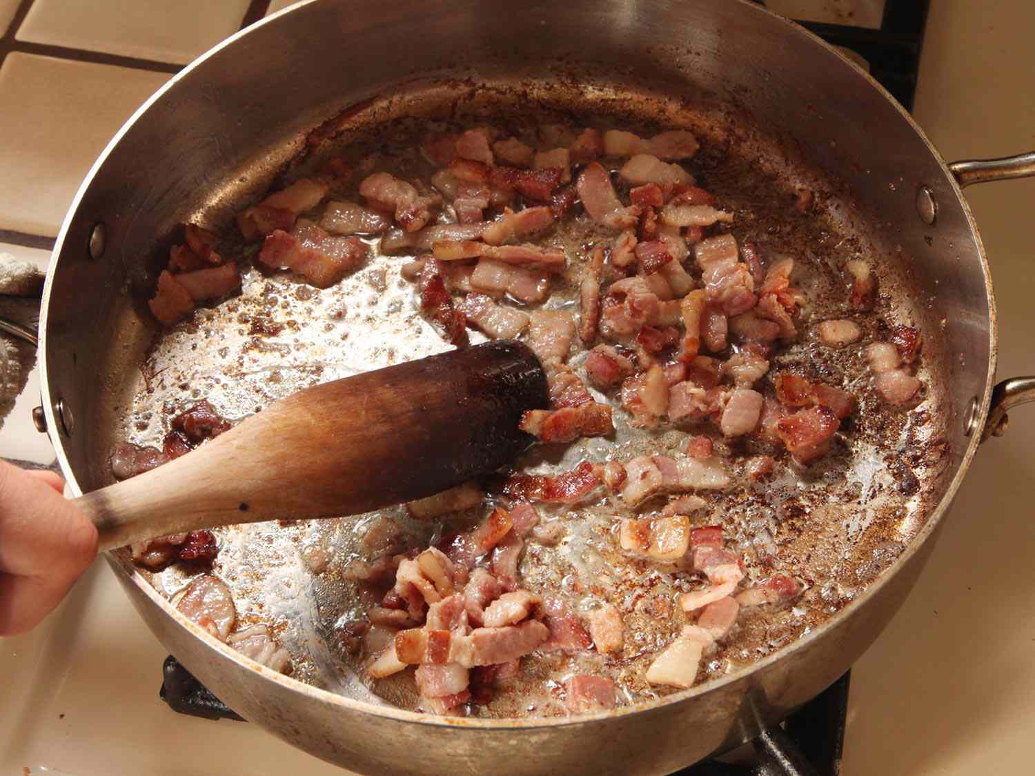 Crisp pieces of bacon being stirred in pan with wooden spoon