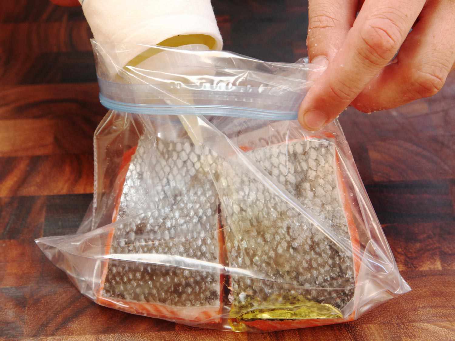 Close up photo of adding olive oil with a squeeze bottle to a zipper-lock bag with two salmon fillets before cooking sous vide.