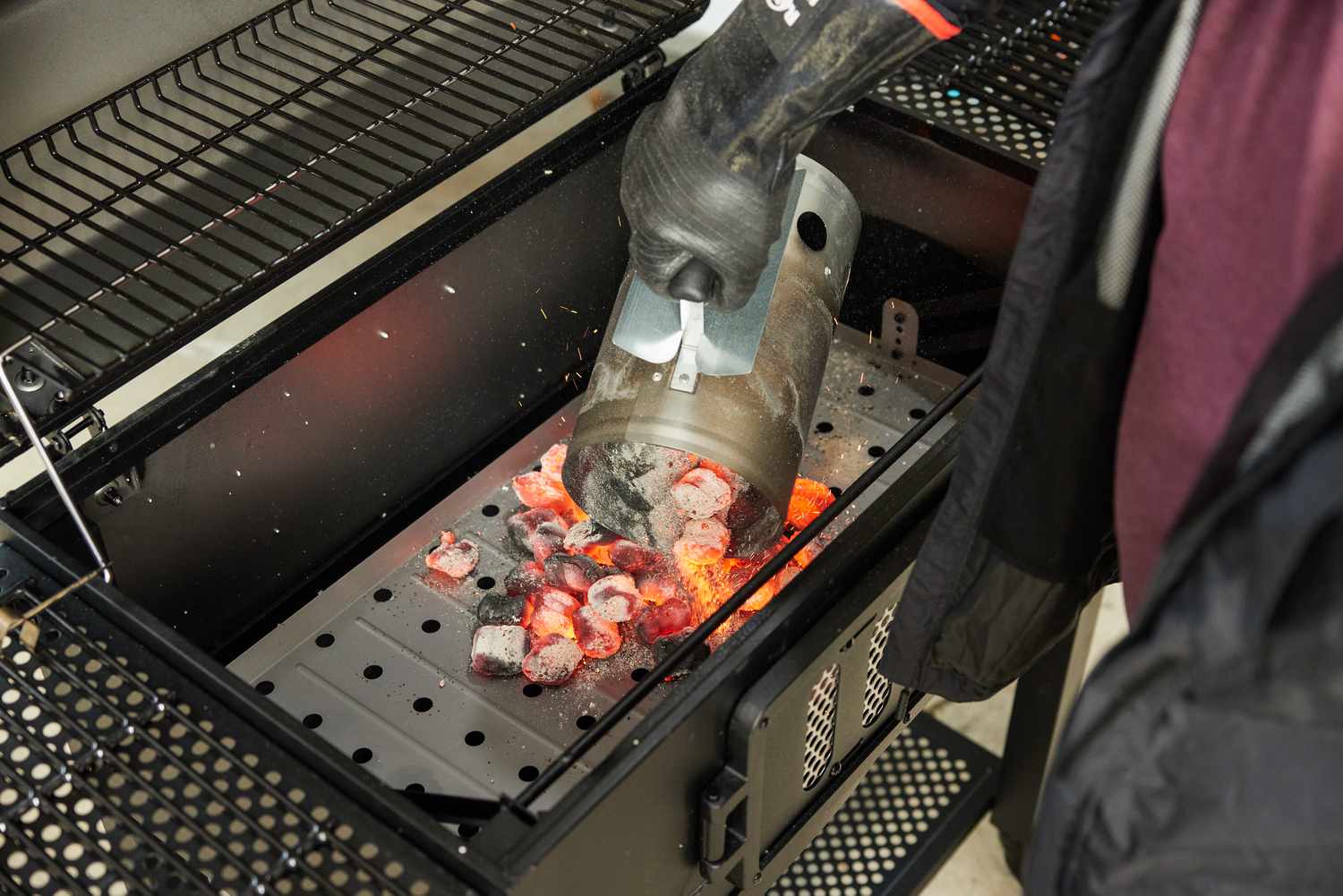 a person using a chimney starter to add charcoal to a grill