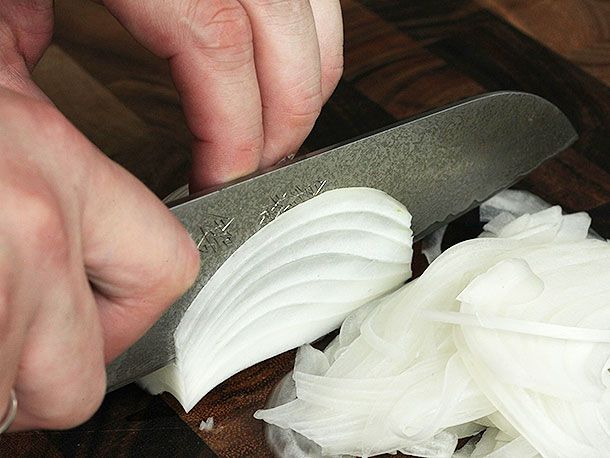 A close-up of a knife slicing an onion.