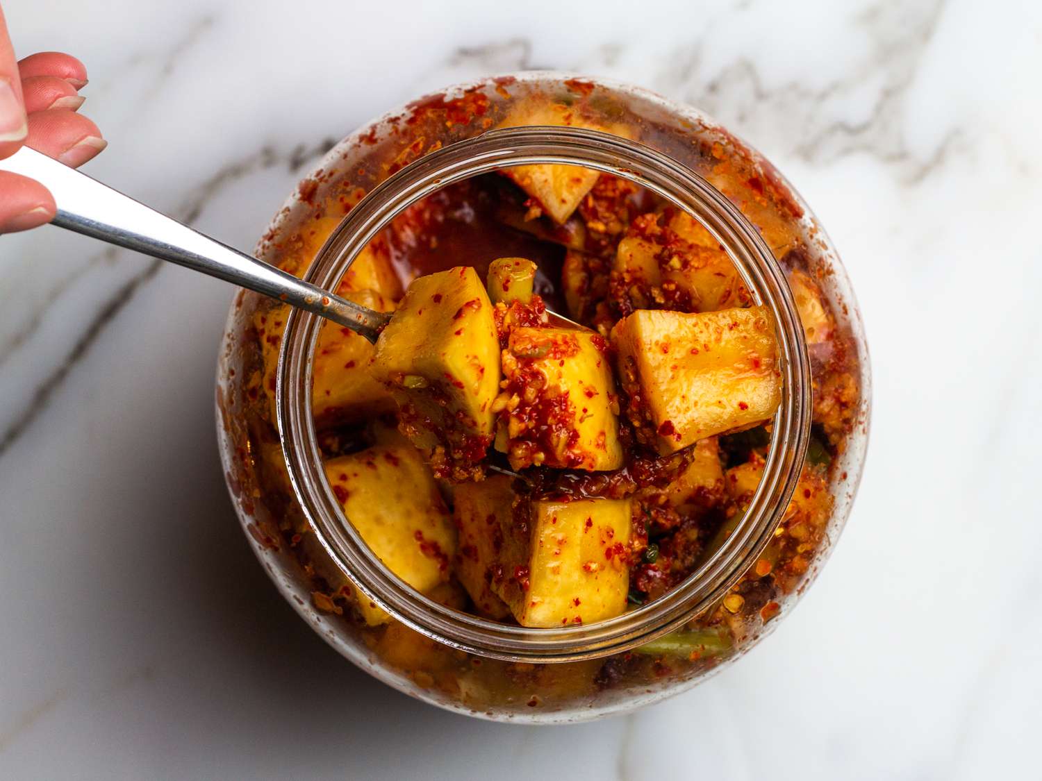 an overhead view of kkakdugi being stirred in jar with a spoon while it continues to ferment