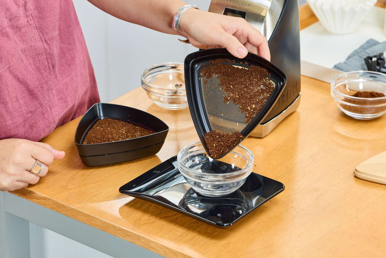 A person measures the weight of beans ground in the Baratza Virtuoso+ Conical Burr Coffee Grinder