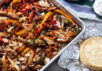 Sheet Pan chicken fajitas with a stack of tortillas nearby.