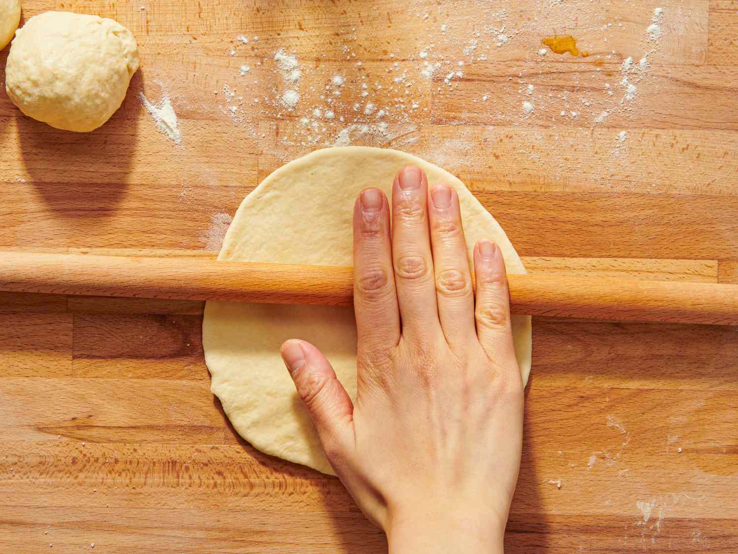 Rolling dough with a wooden rolling pin on a wooden surface