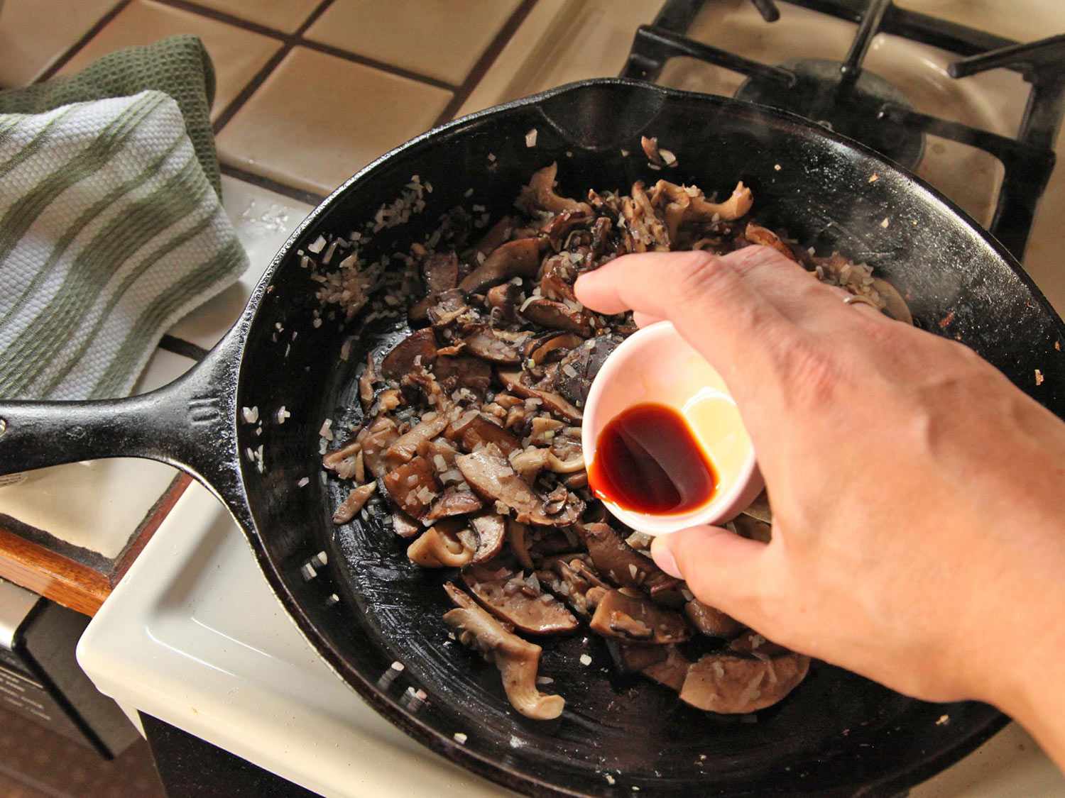 Adding soy sauce to a cast iron skillet of well browned mushrooms. 