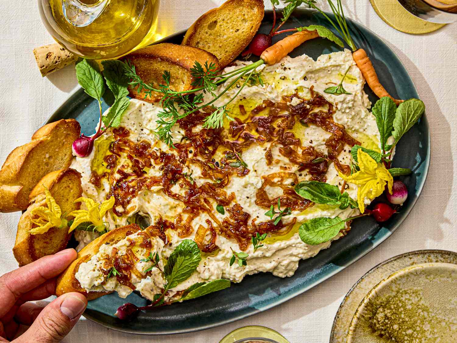 Savory whipped ricotta dip with garnishes surrounded by toasted bread slices and fresh vegetables served on a platter